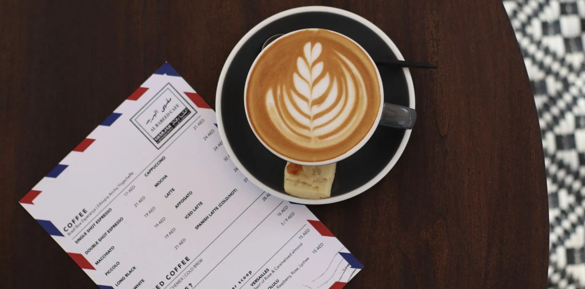 Flat white with latte art beside the Al Bareed coffee menu